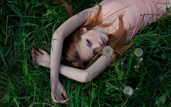 Redhead woman lying in grass with dandelions