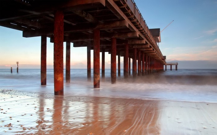Long pier with red supports over the ocean at sunset