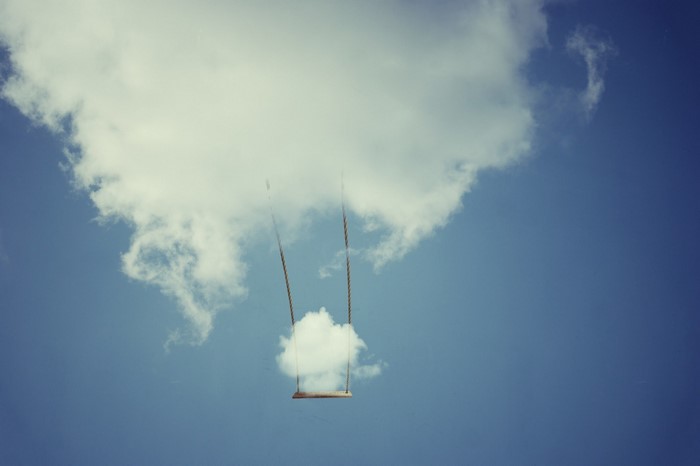 A swing hanging from clouds in a blue sky