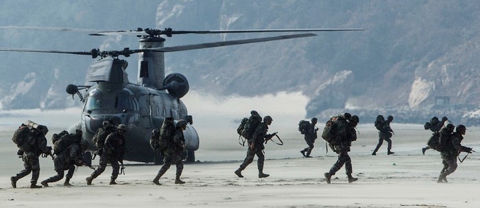 Soldiers disembarking from a Boeing CH-47 Chinook helicopter on a beach