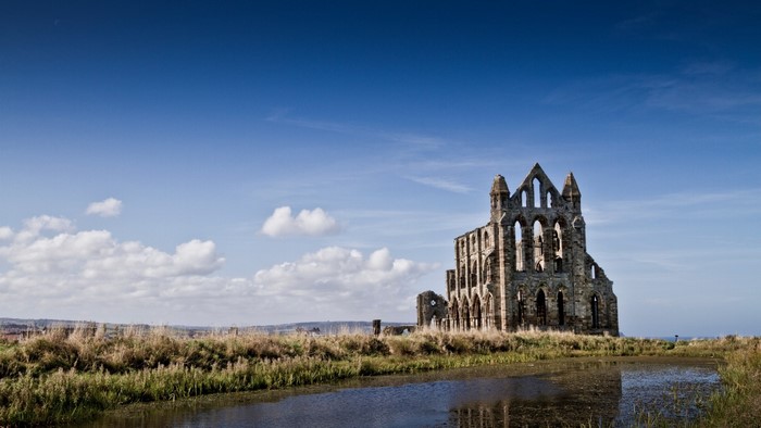 Whitby Abbey ruins by a waterway under a blue sky