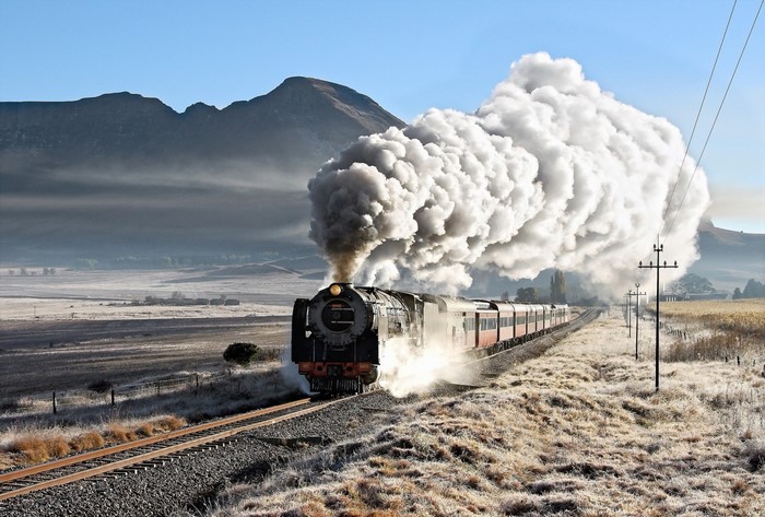 Steam train with large smoke plume in a mountainous landscape