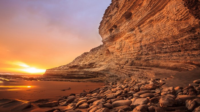 Sunset over a rocky coastline with layered cliffs
