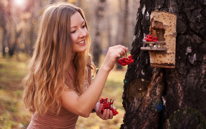 Woman feeding berries to a birdhouse on a tree