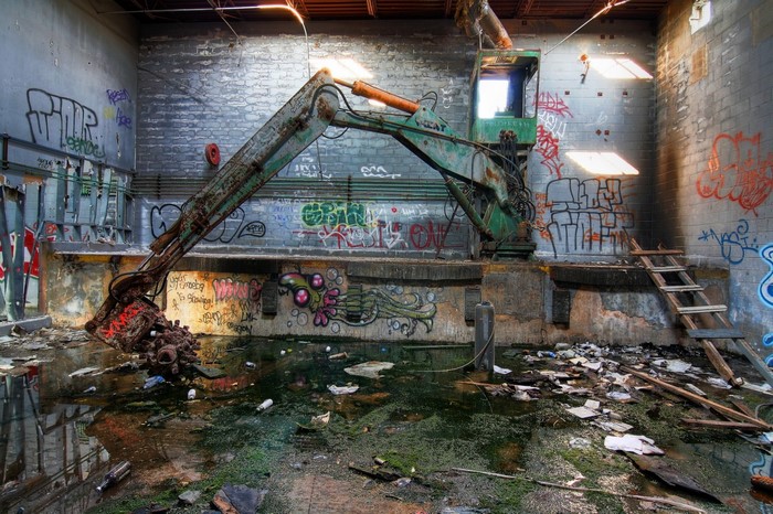 Graffiti-covered abandoned building with excavator and water