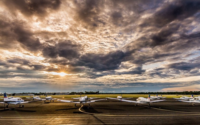 Airplanes parked on tarmac at sunset with dramatic clouds