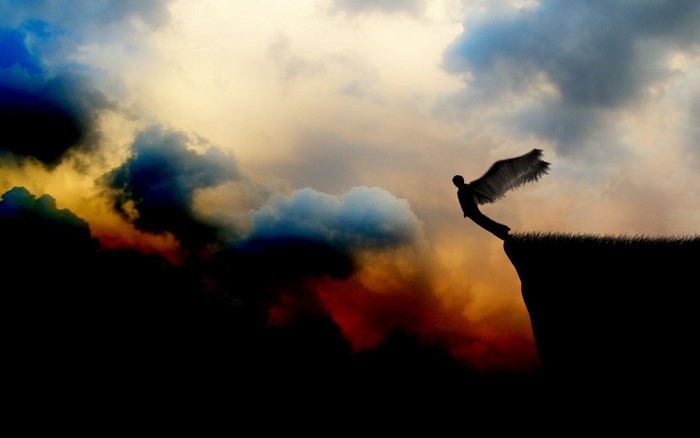 Silhouette of a winged figure leaping from a cliff at sunset