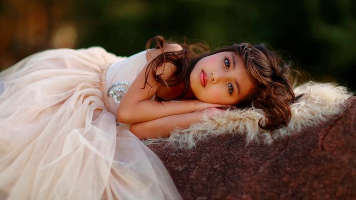 Young girl in a light pink dress lying on a rock