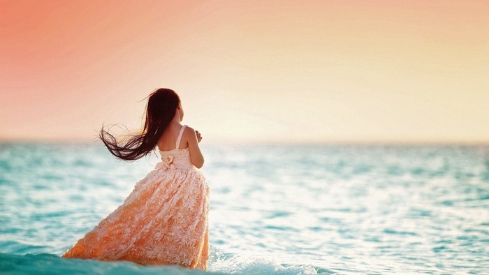 Girl in a dress by the sea at sunset