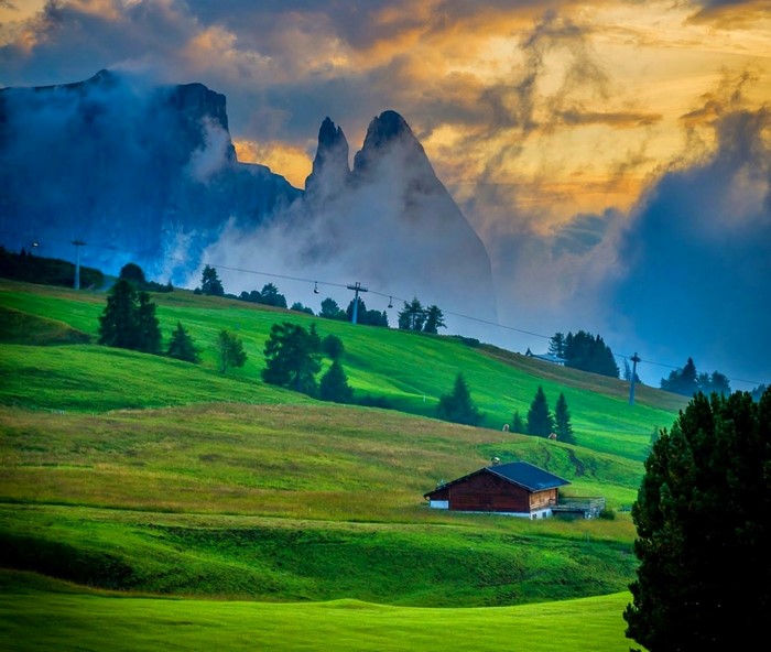 Cabin on a grassy hill in the Dolomites at sunset