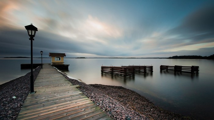 Wooden pier with a small yellow house and lampposts on a lake at dusk