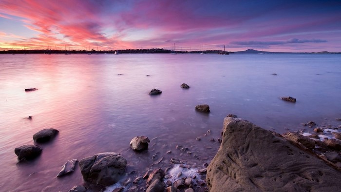 Sunset over water with rocks and distant land