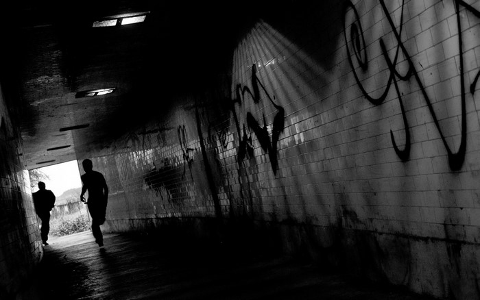 Two figures running through a graffiti-covered tunnel at night