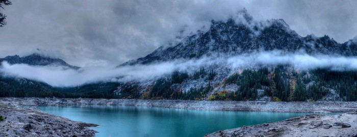 Misty mountains over a turquoise lake with pine trees