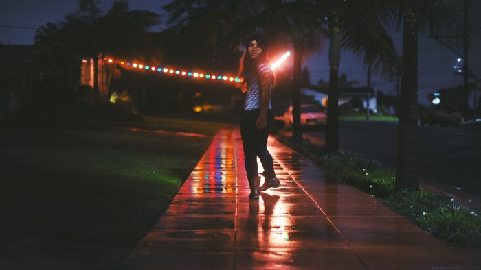 Woman with light stick on wet sidewalk at night