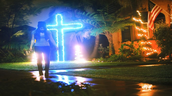 Girl walks past a large illuminated cross at night