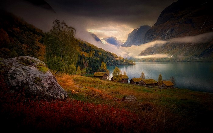 Autumnal landscape with cabins by a lake and mountains