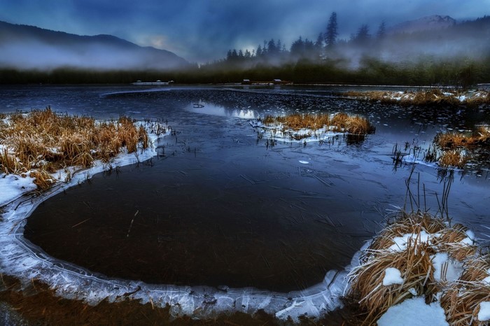 Frozen lake with reeds and misty mountains