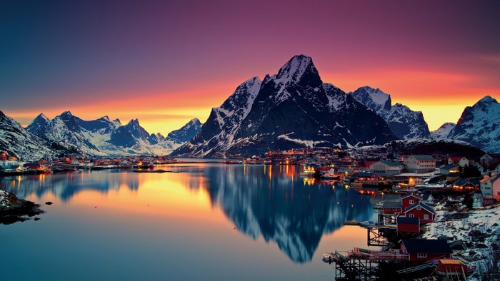 Village by mountains at sunset with lake reflection