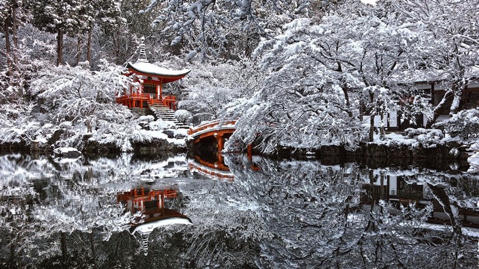 Japanese temple and bridge reflected in a snow-covered pond