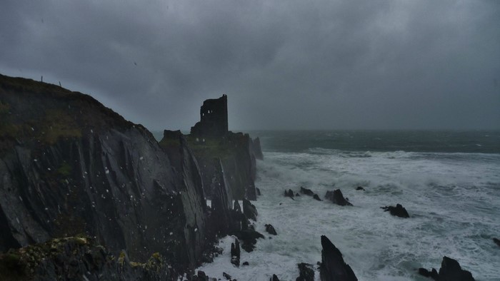 Ruined castle on a cliff overlooking a stormy sea in Ireland