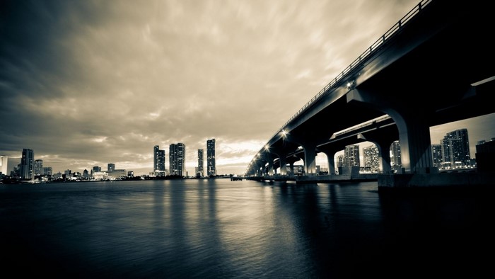 Monochrome cityscape with bridge over water at dusk