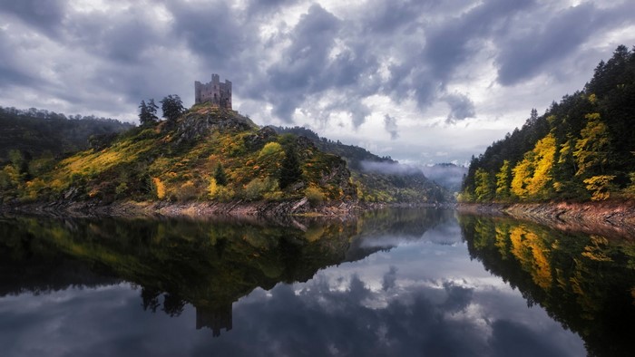 Castle ruins on a hill reflected in a lake during autumn