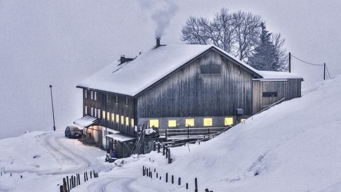 Snowy wooden building with smoke from chimney in winter