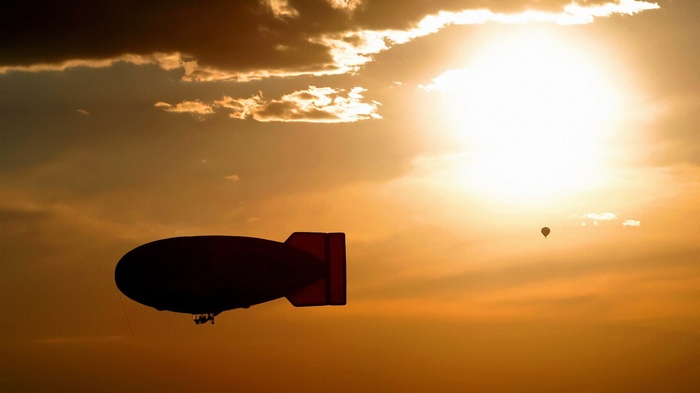 Blimp and hot air balloons at sunset