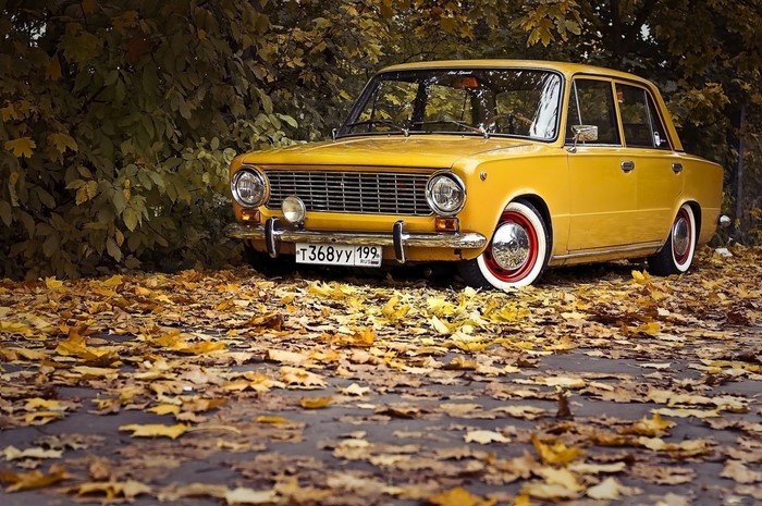 Yellow classic sedan car on a road covered in autumn leaves