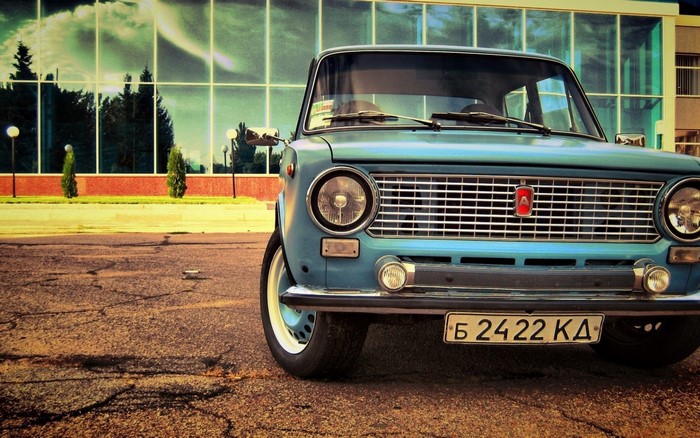 Blue LADA classic car parked in front of a modern building