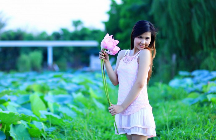 Woman holding a pink lotus flower in a field of lotus pads