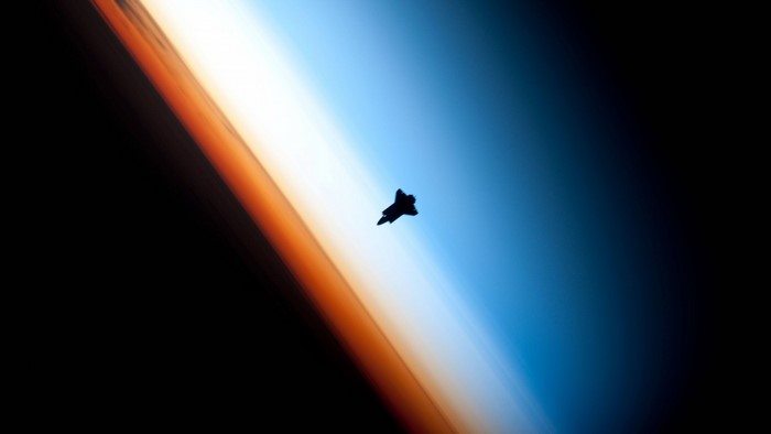Space Shuttle silhouette against Earth's atmosphere