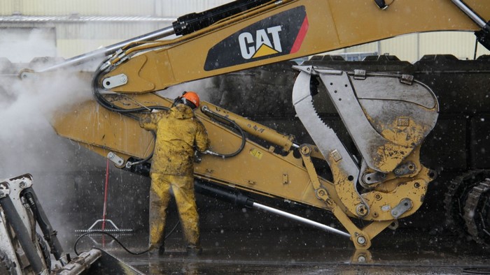 Worker pressure washing a CAT excavator