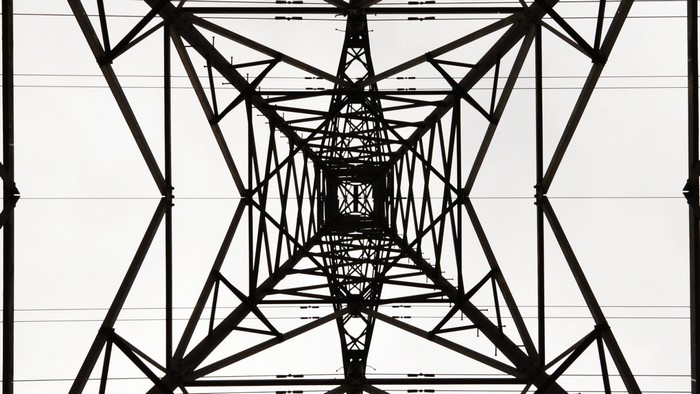 Symmetrical view of a transmission tower against a bright sky