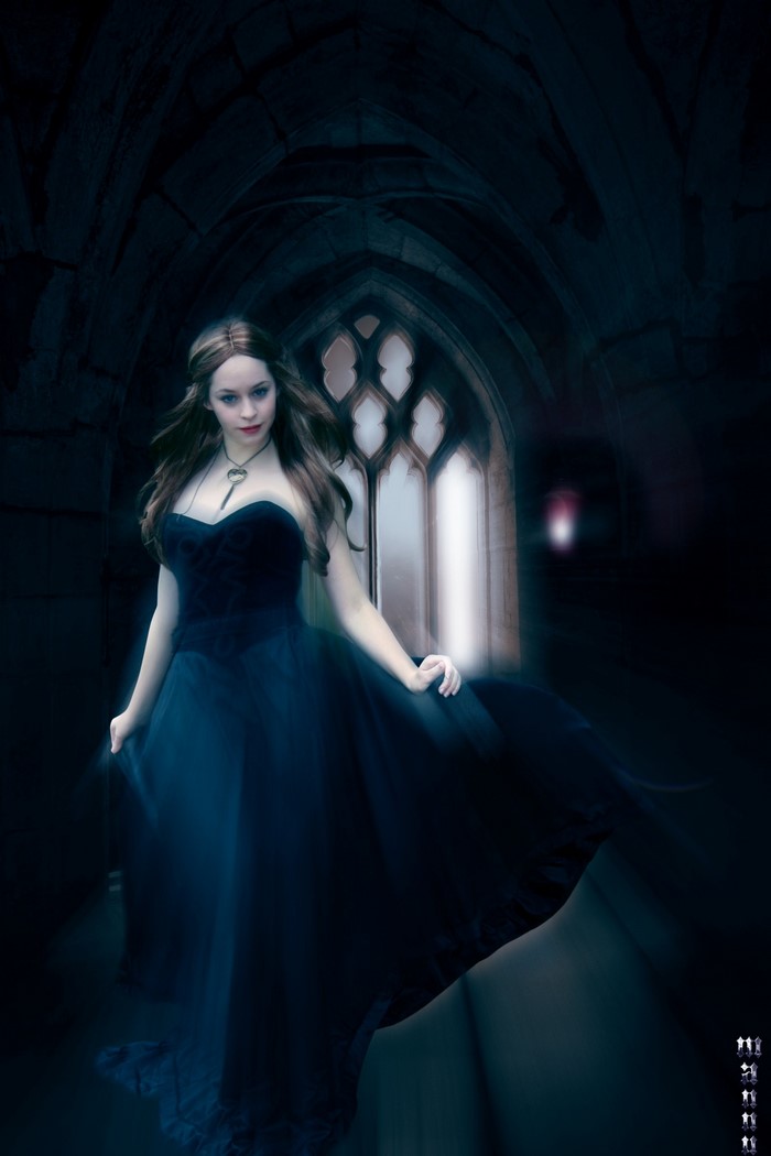 Woman in a dark blue gown in a gothic hall