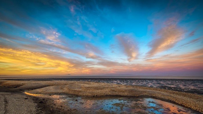 Sunset over a sandy shore with colorful clouds and reflections