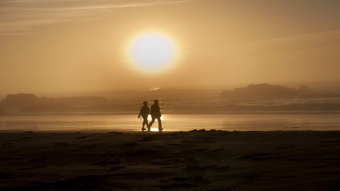 Two people walking on a beach at sunset