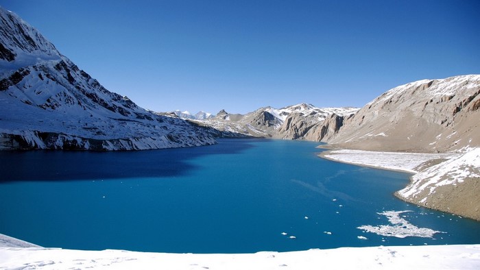 Blue lake surrounded by snow-capped mountains under a clear sky
