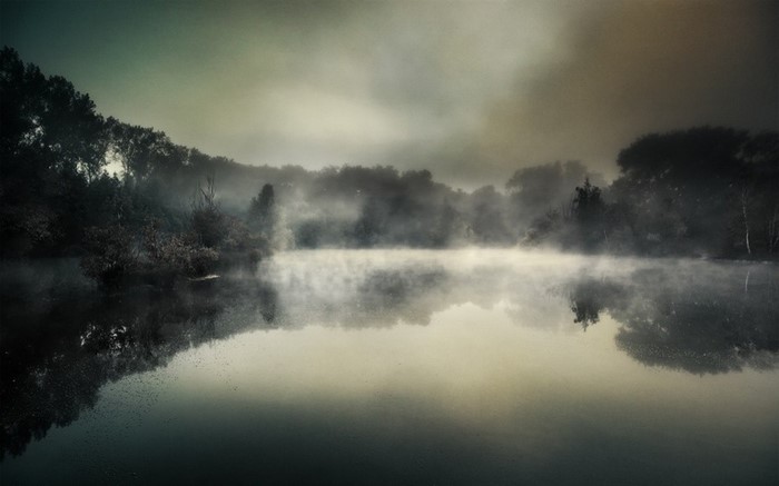 Misty lake at dawn with trees and reflections