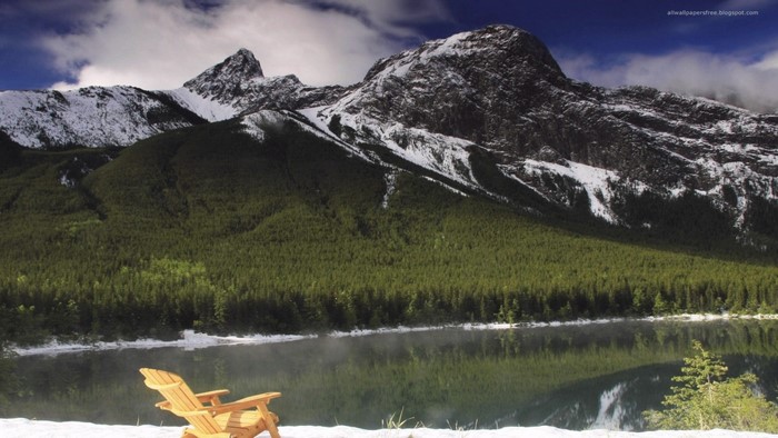 Wooden chair by a lake with snow-capped mountains
