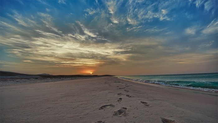 Sunset over a sandy beach with footprints and ocean waves