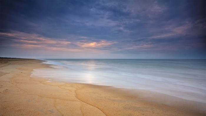 Beach at sunset with ocean waves and clouds
