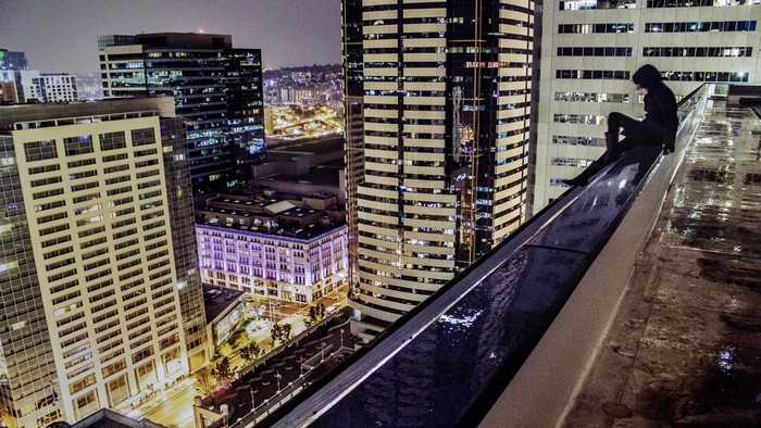 Person sitting on a skyscraper edge at night
