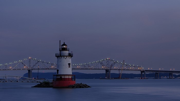 Lighthouse and bridge over water at dusk