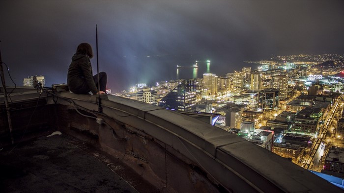 Person sitting on a rooftop overlooking a city at night