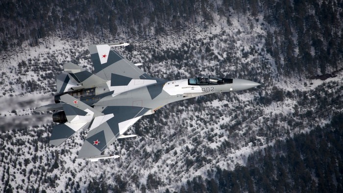 Sukhoi Su-35 fighter jet flying over a snowy forest