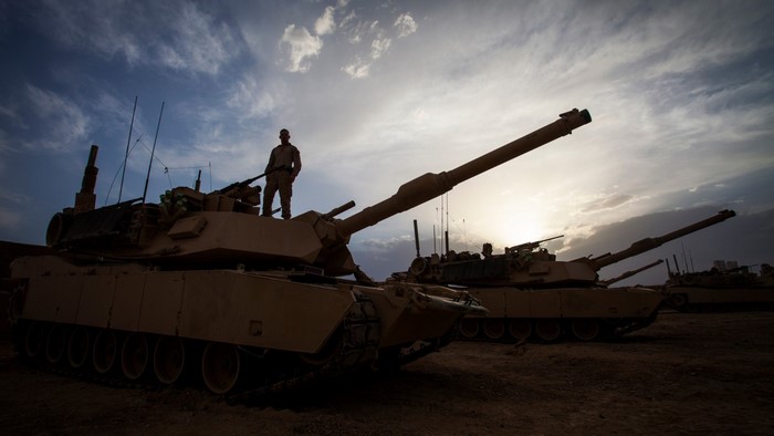 Soldier standing on M1 Abrams tanks at sunset