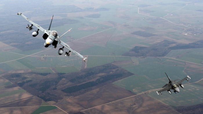 Two fighter jets flying over rural landscape