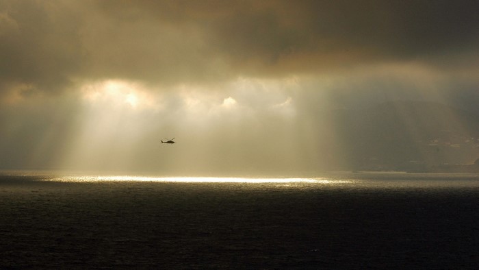 Helicopter flying over the sea during a sunbeam through clouds
